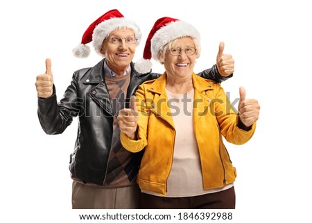 Happy elderly man and woman wearing leather jackets, santa claus hats and gesturing thumbs up isolated on white background