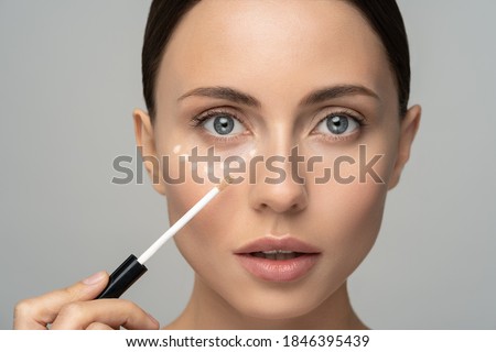 Close up of woman with natural makeup applying corrector on flawless fresh skin, doing make up. Girl after shower put concealer under eye area. Beauty face, skin care. Copy space, banner, advertising. Royalty-Free Stock Photo #1846395439