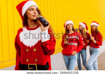 company of young beautiful women in Christmas sweaters and Santa Claus hats drinks drinks while walking around the city against