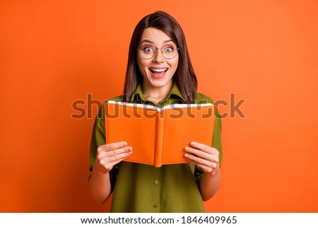 Photo portrait of surprised brunette girl keeping book laughing isolated on vivid orange color background