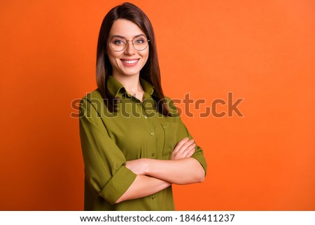 Photo portrait of cheerful girl with folded hands wearing glasses smiling isolated on vibrant orange color background with blank space
