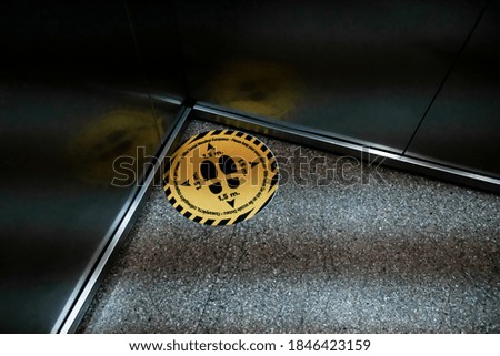 Yellow warning mark on the floor in an elevator. Protecting guests from coronavirus spreading in a hotel. Social distancing during global pandemic. Bright sticker with footprint symbol in a lift.