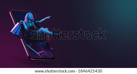 Beautiful woman inviting for shopping right from device screen, black friday, sales concept. Flyer. Cyber monday and online purchases, negative space for ad. Finance and money. Dark neon background. Royalty-Free Stock Photo #1846425430