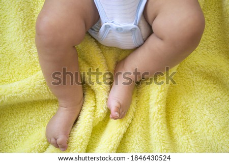 little feet. Newborn baby belly and legs in diaper, lying on yellow blanket, top view. The legs of a newborn baby. feet of baby wearing diapers lying on the bed at home. baby in bodysuit.