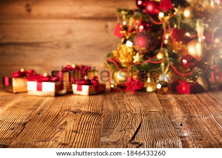 Golden presents with red ribbon under decorated Christmas tree. Wooden background and table. 