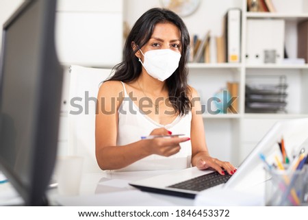 Portrait of brazilian businesswoman discussing financial report or explaining business task in office in disposable face mask. Pandemic precautionary concept