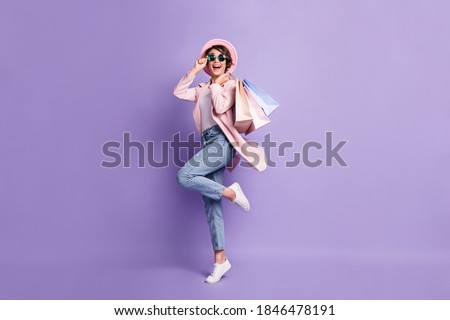 Full size photo of positive pretty girl jump hold purchases wear glasses coat jeans shoes isolated on purple background Royalty-Free Stock Photo #1846478191