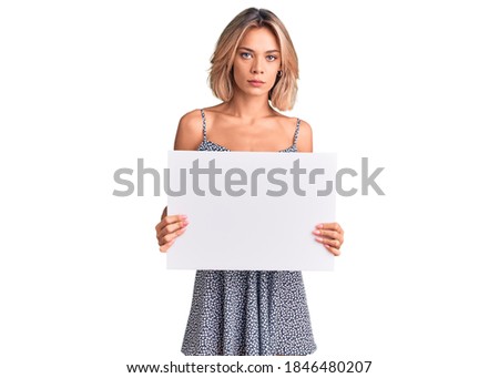 Beautiful caucasian woman holding blank empty banner thinking attitude and sober expression looking self confident 