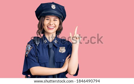Young beautiful girl wearing police uniform with a big smile on face, pointing with hand and finger to the side looking at the camera. 