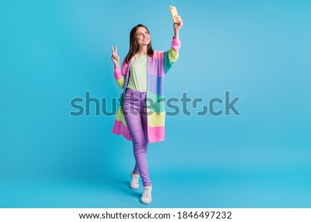 Full size photo of brown haired blogger girl make v-sign take selfie record video hold phone wear purple pants isolated on blue color background Royalty-Free Stock Photo #1846497232