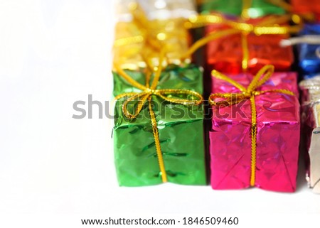 Shiny multicolored boxes with gifts, tied with a golden ribbon, lie on a white background. Festive packaging and surprise. Christmas morning. Close-up. Macro. Shallow depth of field