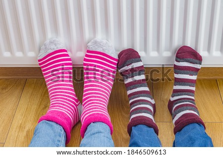 Family wearing colorful pair of bright winter socks warming cold feet in front of heating radiator in winter time. Electric or gas heater at home. The symbolic image of the heating season at home.