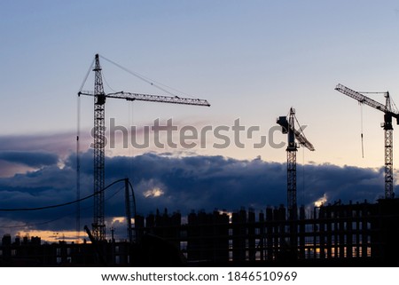 Three cranes and an unfinished residential skyscraper. Dramatic sky dusk evening landscape. Residential building construction