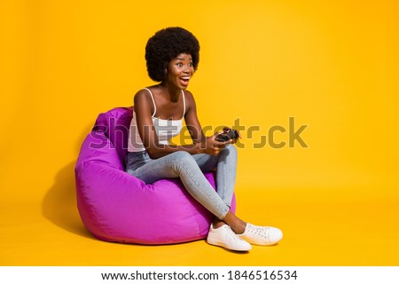 Photo of adorable attractive young lady wear casual outfit sitting beanbag enjoying playstation game isolated yellow color background
