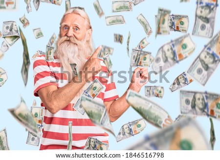 Old senior man with grey hair and long beard wearing striped tshirt smiling and looking at the camera pointing with two hands and fingers to the side.