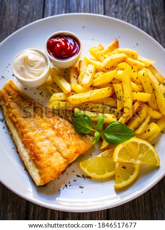 Fish dish - fried cod fillet with French fries and vegetable salad on wooden table 