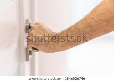 Photo of a male hand holding a metal handle of a white door.