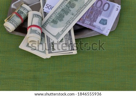 On a green background on a metal tray are banknotes of dollars and euros.
