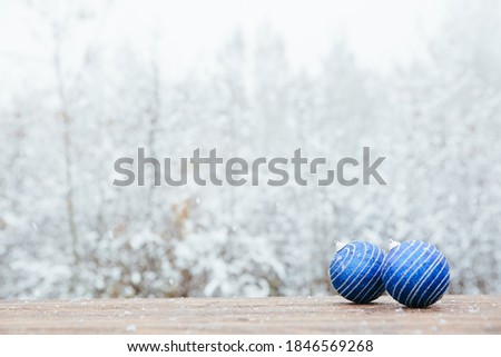 Beautiful Christmas bauble decorations lie on the wooden table over snow covered forest background. .