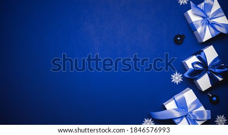 Gift boxes cyan. White gifts with cyan ribbon, New Year balls and winter tree in Christmas composition on dark blue background for greeting card. Xmas backdrop with space for text.