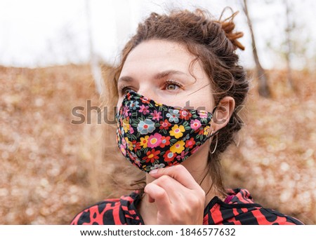 Beautiful thirty-year-old woman in colored mask outdoors.