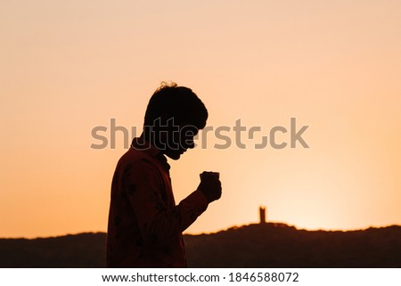 Silhouette of an Indian kid holding tea cup in front of the hill during the sunset