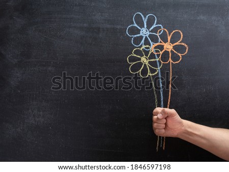 Flowers on a chalkboard, hand holding painted flowers.