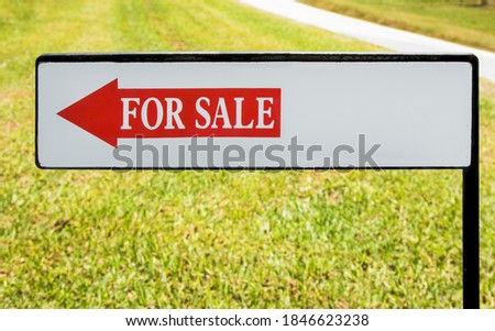 Real estate FOR SALE sign with lawn and sidewalk background.