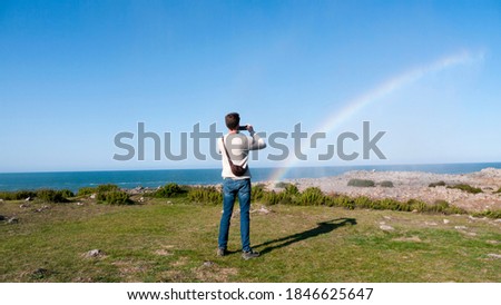 Young man taking a picture to a rainbow formed in natural water jets