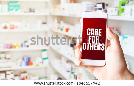 hand holding smart phone in pharmacy drugstore. Text CARE FOR OTHERs