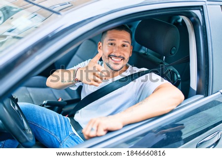 Young hispanic man smiling happy doing ok sign driving car.