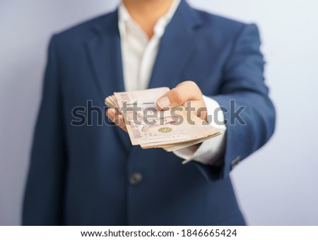 Money in thailand hold on hand business man wearing a blue suit. Filed and put and give to me. THB, thai baht, exchange money on white background. Business finance and bank employee Concept. Royalty-Free Stock Photo #1846665424