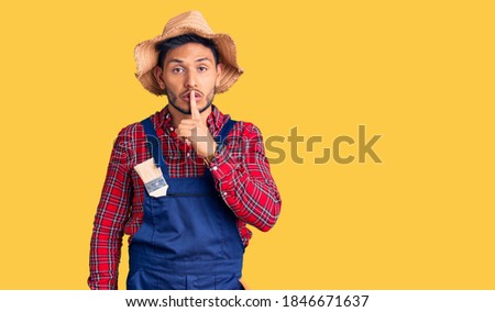 Handsome latin american young man weaing handyman uniform asking to be quiet with finger on lips. silence and secret concept. 