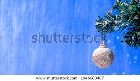 Christmas ball with glitter covered in snow hanging on the fir branch against the colorful blue background. Banner with copy space
