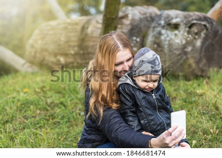 Young red haired mother with her little son check the selfie taken together in sunny autumn day