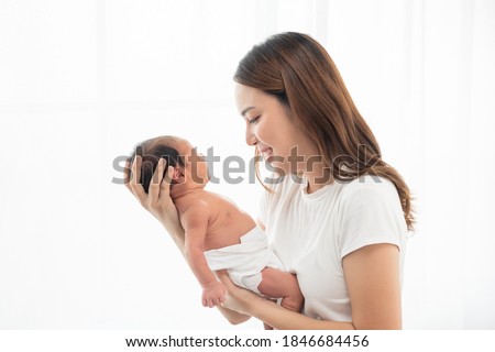 Pretty asian woman smile and holding a newborn baby in her arms. Happy family. Asia mother lifting her adorable infant baby on white. love people concept
