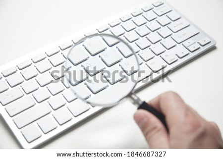 Hand holding magnifying glass with computer keyboard. Searching internet