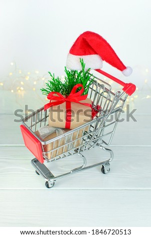 Shopping cart with gift small boxes on a white wooden background. Christmas and New Year sale. Seasonal online shopping xmas, noel. Vertical photo