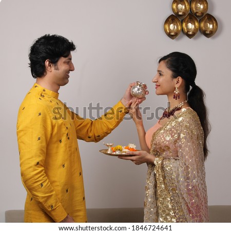 Good looking husband performing Karwa Chauth traditions of offering water to her fasting wife in traditional wear. Royalty-Free Stock Photo #1846724641