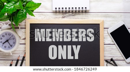 The word MEMBERS ONLY written on a black background near pencils, a smartphone, a white notepad and a green plant in a pot