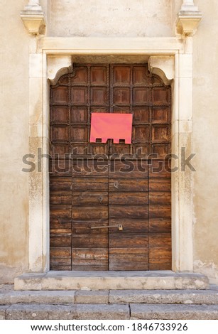 Old wooden portal of an ancient church, with an empty red banner hung on it