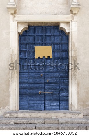 Old wooden blue-colored portal of an ancient church, with an empty yellow banner hung on it