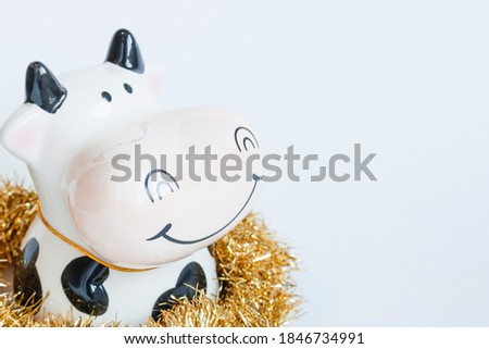 Clay figure of a bull in white and black color decorated with a Christmas garland on a white background. New year of the bull