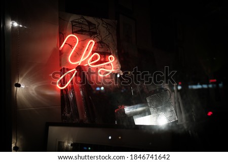 Say Yes to everything - neon light saying yes in the store through a window with a lot of pictures