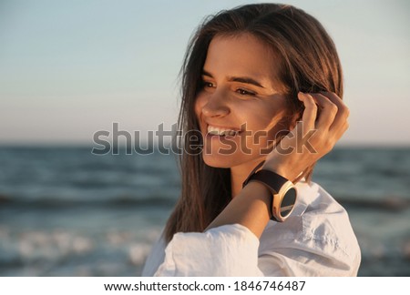 Young woman wearing smart watch on beach at sunset