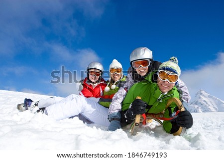 A cheerful family smiling at the camera as they are lying together in the snow with a sled