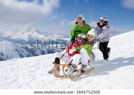 An adventurous family having fun in the snow as mother and daughter being pushed downhill through the snowy slope while riding on a sled