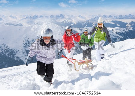A fun and happy family running together in the snow while pulling a sled uphill on a steep slope