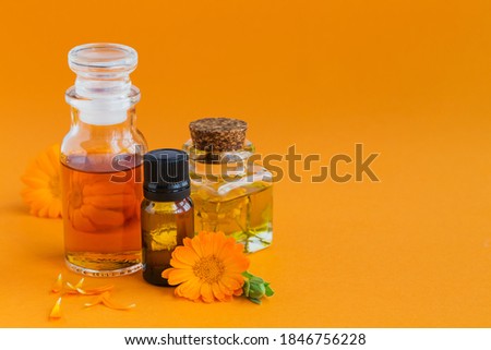 Calendula products. Bottles of cosmetic, aromatic or essential oil and fresh calendula flowers on orange background. Aromatherapy, spa and wellness concept