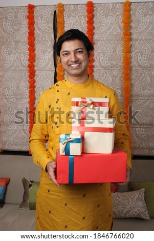 Young happy Indian man wearing traditional  holding gift boxes.